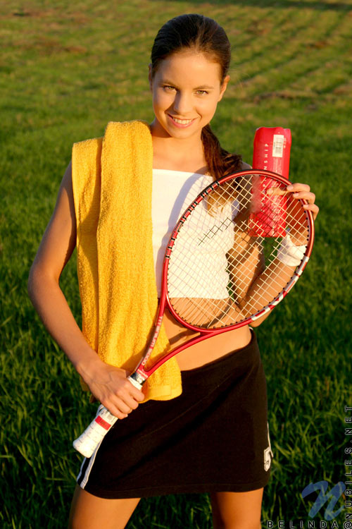 A perfect sporty teen chick posing with her tennis racket on grassy playground