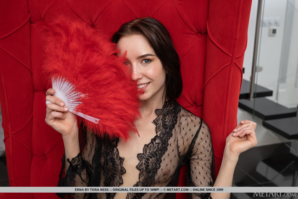 Erna teasingly uses the red feather fan as she flaunts her slim figure and hairless cunt on the red big chair.